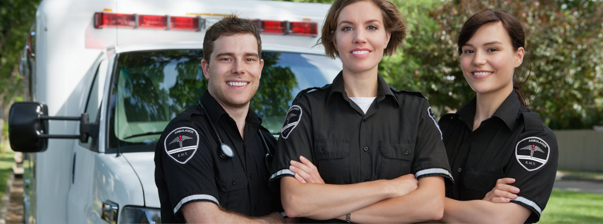Group of three paramedics standing in front of ambulance with smile