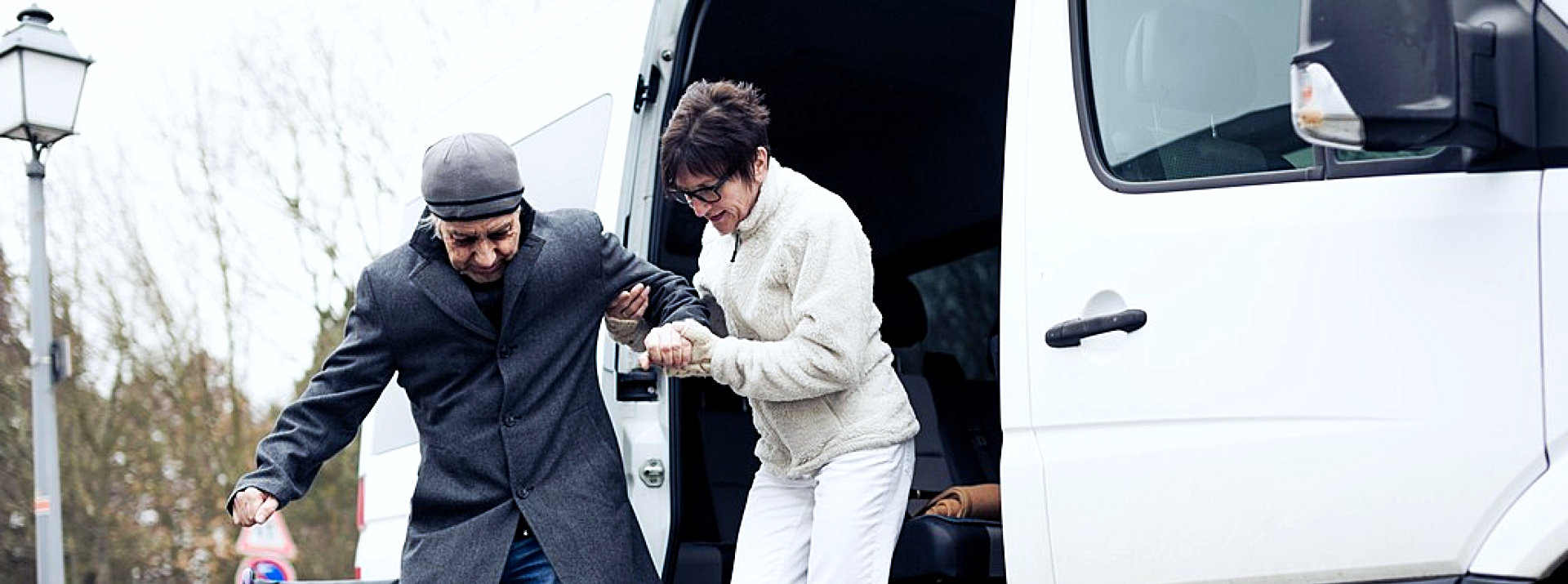 woman helping a senior man getting of the van